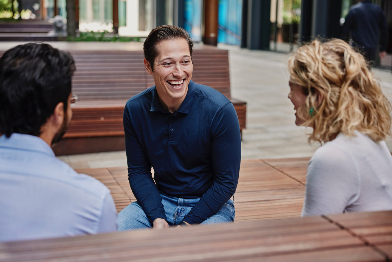 Photo of Grant Aarons sitting on a bench outside talking to two people